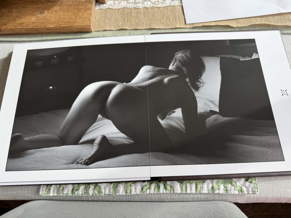 Artistic boudoir album showing black-and-white photo of woman posing on bed in soft light with dramatic shadows.