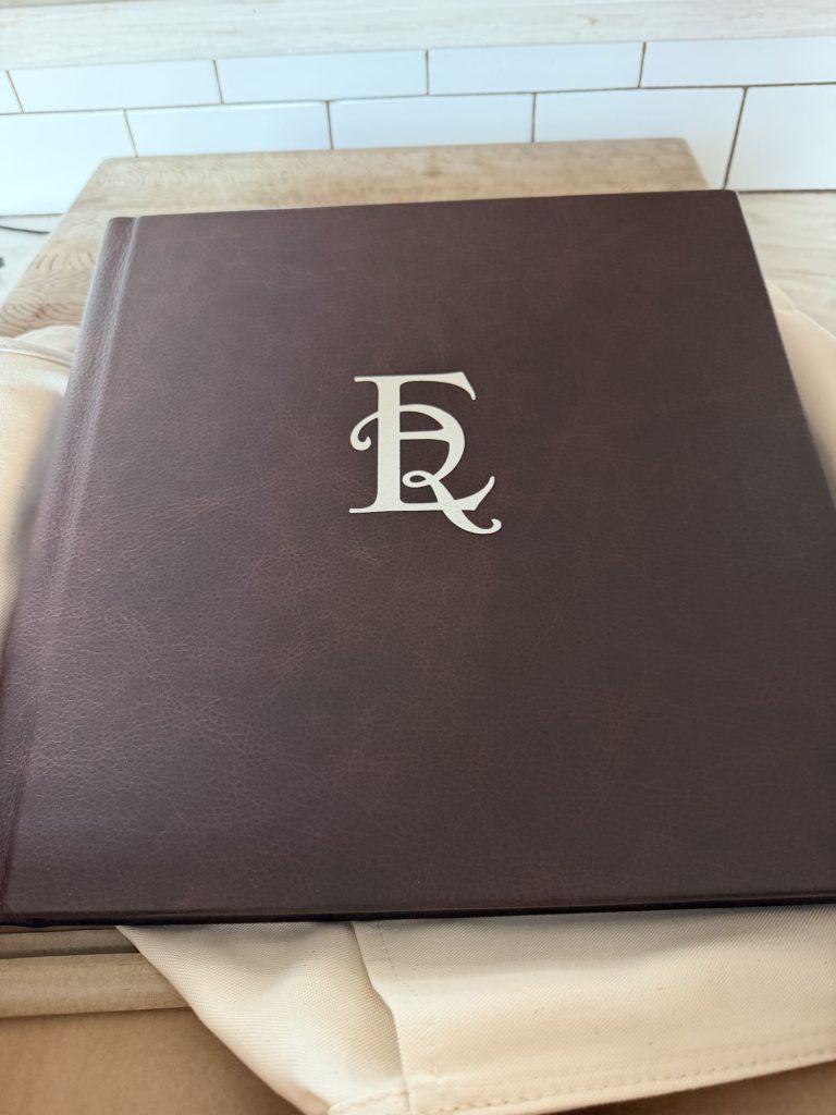 JG Boudoir Album featuring closed rich brown leather cover with large ornate white monogram in soft lighting.