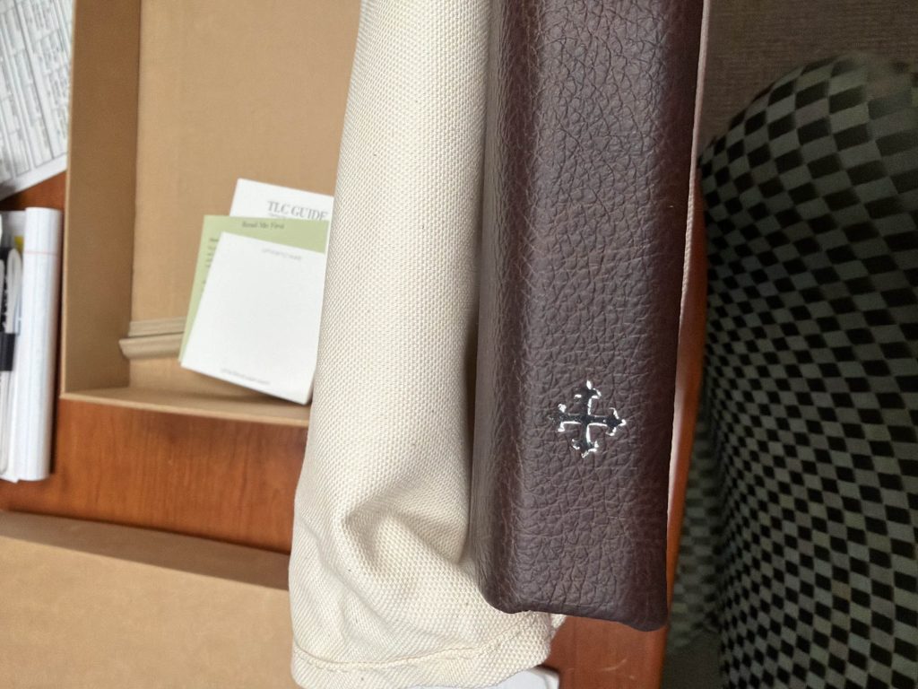 JG Boudoir Album With Custom Publishers Mark close-up of brown leather spine with ornate silver emblem in soft lighting.