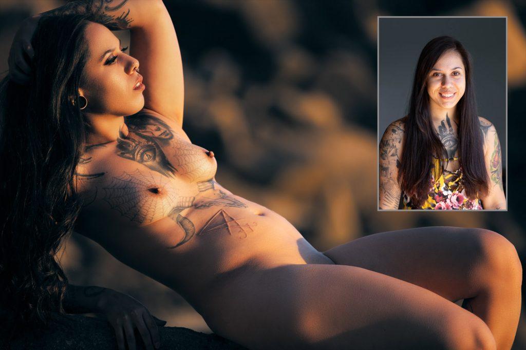 A woman with long dark hair and extensive tattoos reclines gracefully on a rocky surface during her JG Boudoir session. Warm golden lighting illuminates the scene as she poses with one arm raised above her head while gazing to the side. The client before and after image includes an inset portrait in the upper right corner showing the same woman smiling in a colorful floral top before her makeover. 